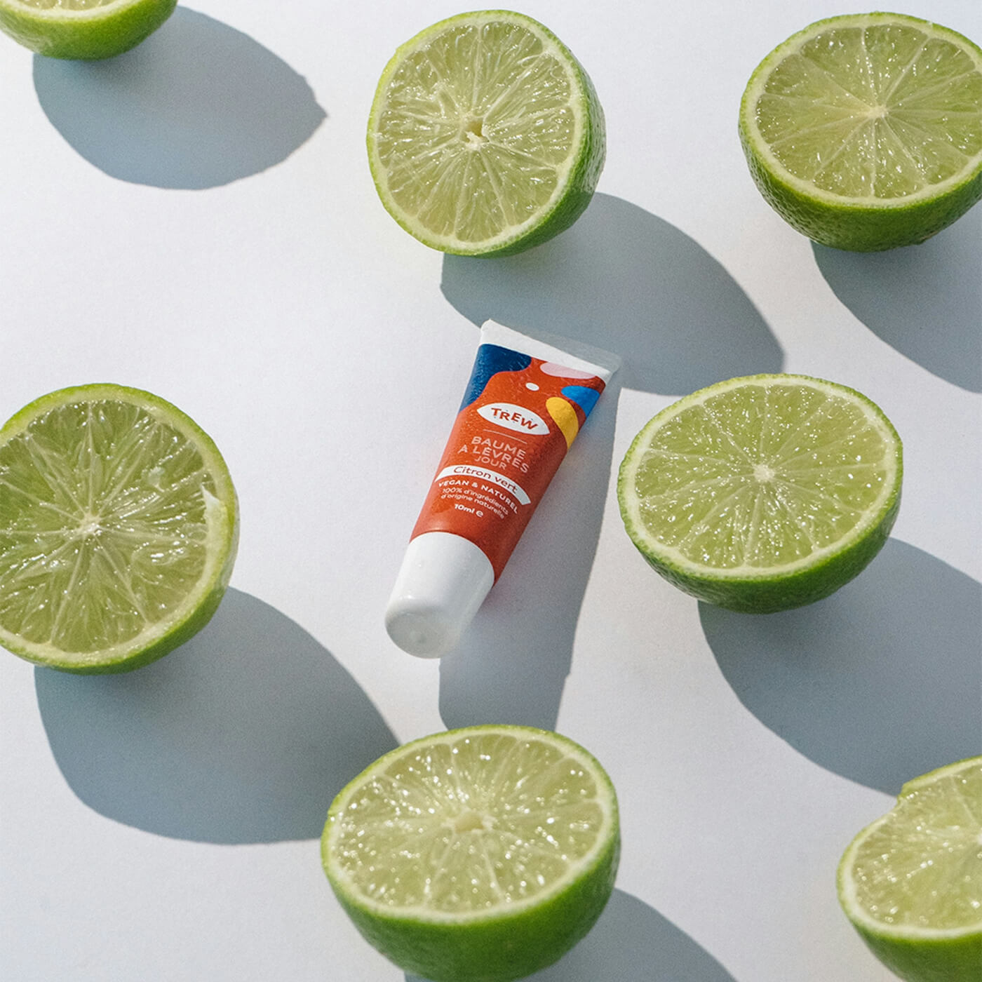 Trew skincare lip balm surrounded by halved limes on white background.