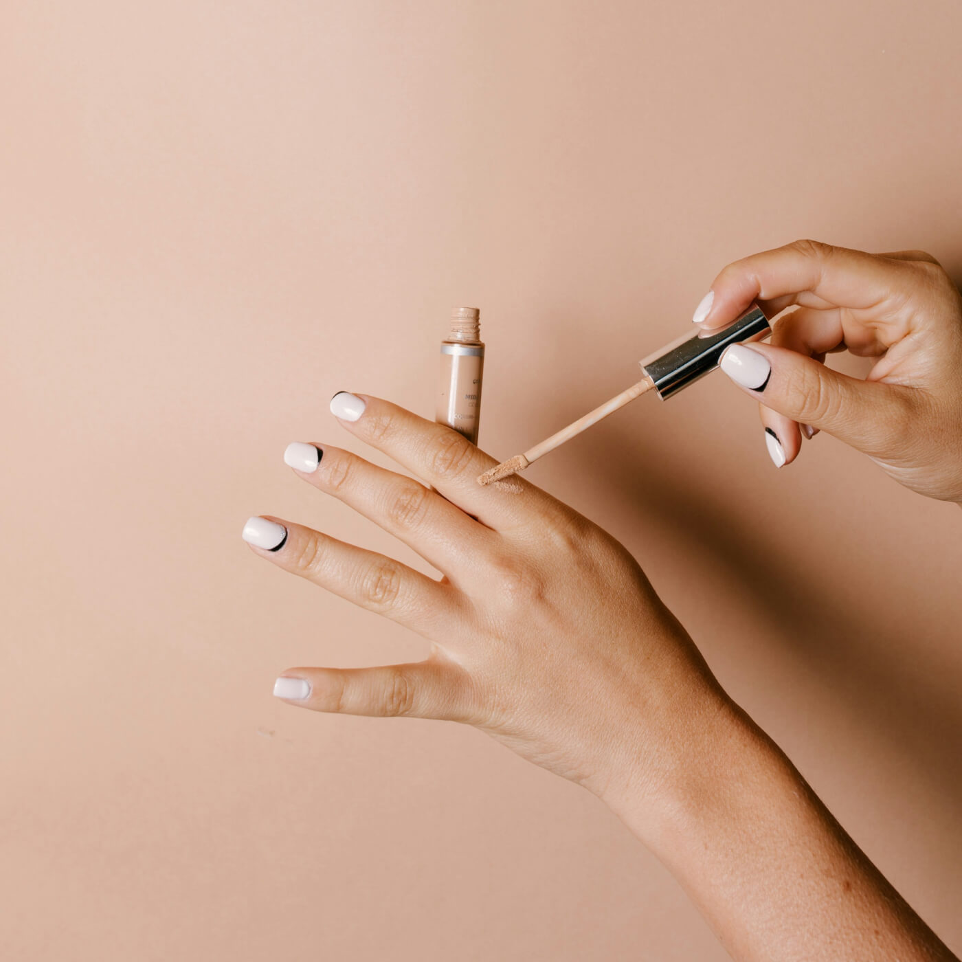 Applying liquid concealer on hand with nude background.