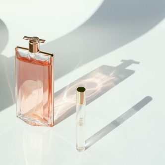 Elegant pink perfume bottle casting a soft shadow beside a small spray vial.
