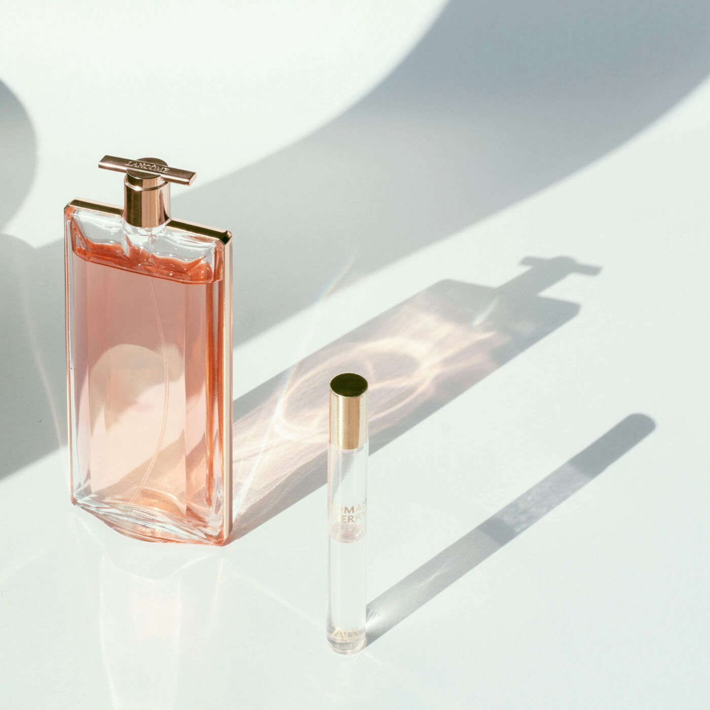 Elegant pink perfume bottle casting a soft shadow beside a small spray vial.