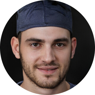 Close-up portrait of a man wearing a navy blue cap with a slight smile.