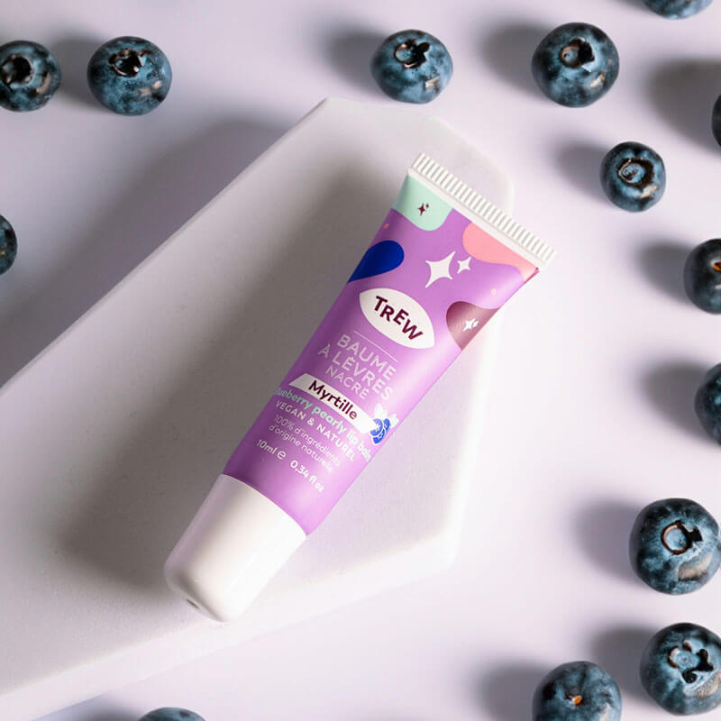 A tube of Trew blueberry lip balm surrounded by fresh blueberries.