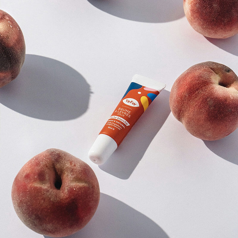 Lip balm tube surrounded by fuzzy peaches on a white surface.