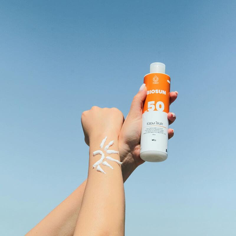 Sunscreen lotion applied in the shape of a sun on a hand against a clear blue sky.