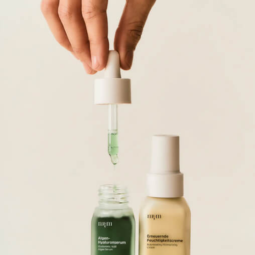 Hand holding a dropper with green liquid over a bottle.