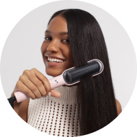 Woman smiling while straightening her long hair with a heated brush.