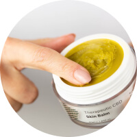 A finger scooping greenish skin balm from a white jar.