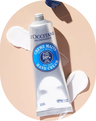 Tube of L'Occitane Shea Butter hand cream with cream spread on a beige surface.