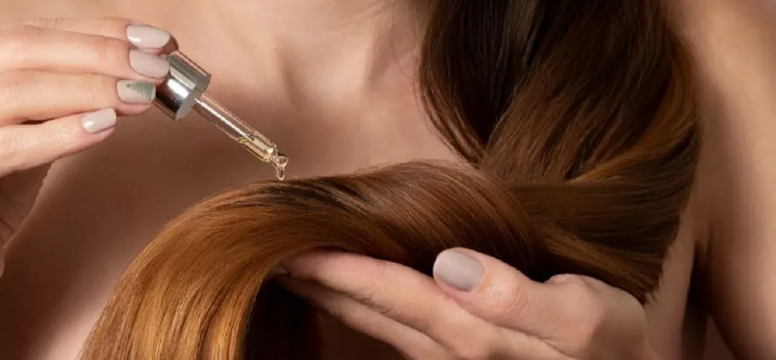 Dropper applying oil to long brown hair